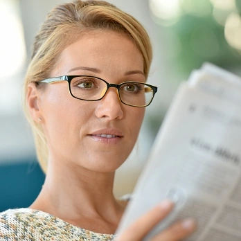 Middle-aged blond woman with eyeglasses reading newspaper